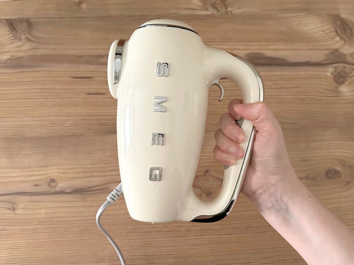 Eine Hand hält den Smeg-Handmixer an dem Griff seitlich in die Kamera