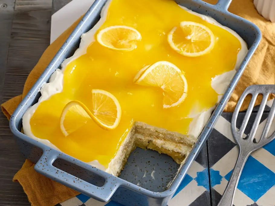 Solero Tiramisu Rezept Eine Auflaufform mit Solero Tiramisu, bedeckt von gelber Fruchtschicht und mit mehreren Zitronenscheiben garniert.