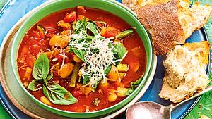 Minestrone mit großen weißen Bohnen, Basilikum und Parmesan in einer grünen Suppenschale. Daneben liegt Ciabatta. - Foto: House of Food / Bauer Food Experts KG