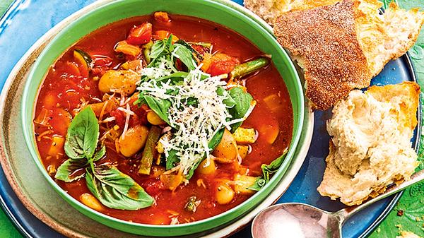 Minestrone mit großen weißen Bohnen, Basilikum und Parmesan in einer grünen Suppenschale. Daneben liegt Ciabatta. - Foto: House of Food / Bauer Food Experts KG