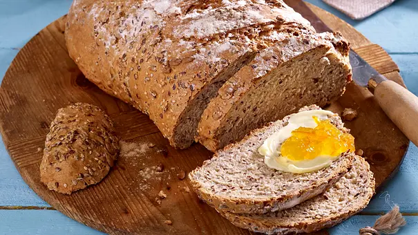 Sonnenblumkern-Brot angeschnitten auf einem Holzbrett, eine Scheibe bestrichen mit Butter und einem Klecks Marmelade - Foto: LECKER @ Bauer Media Group