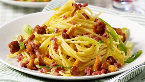 Ein weißer Teller mit Spaghetti, Pfifferlingen, Speckstücken und Lauchzwiebelringen. - Foto: House of Food / Bauer Food Experts KG