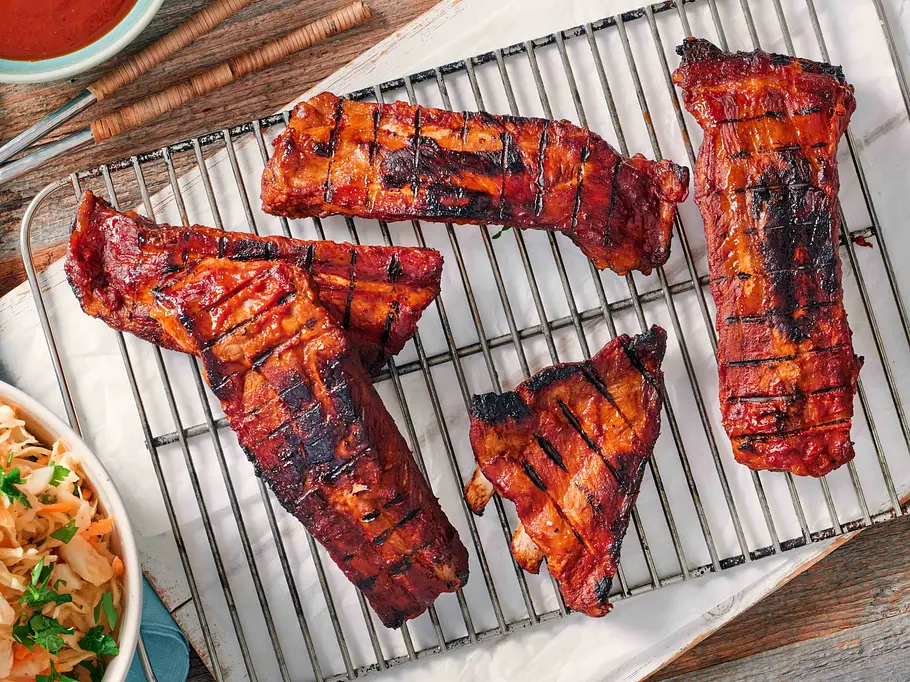 Spareibs grillen Spareribs liegen auf einem Rost, sie sind mariniert und weisen Grillspuren auf.