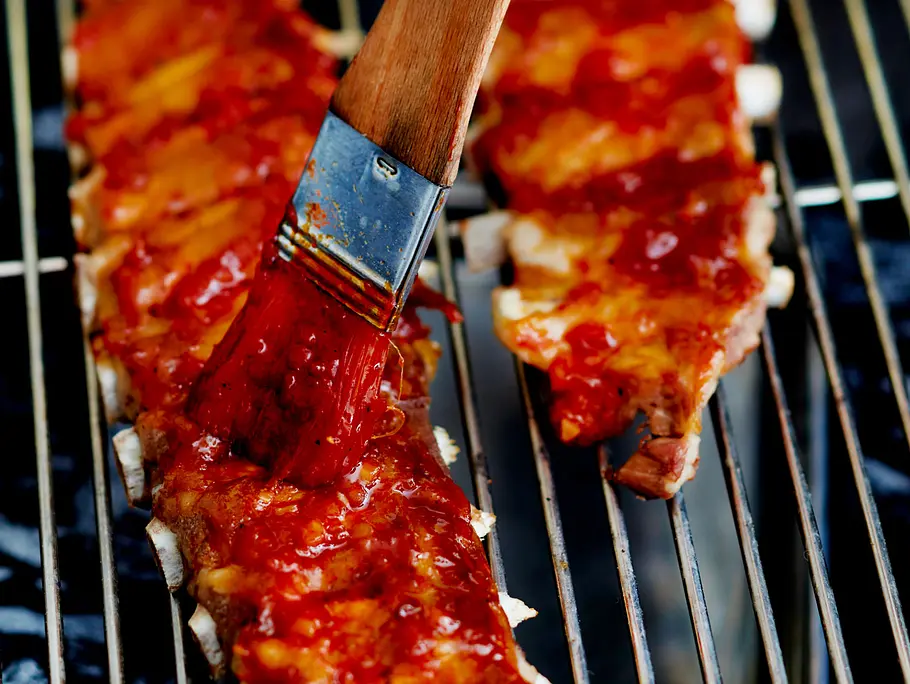 Spareribs auf dem Grill mit Marinade bestreichen. Spareribs auf dem Grill mit Marinade bestreichen.