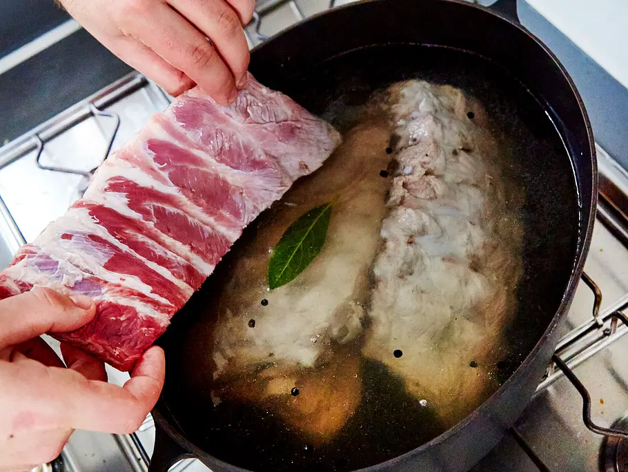 Spareribs zum Grillen vorkochen Rippchen werden in einen Topf mit heißem Wasser gelegt.