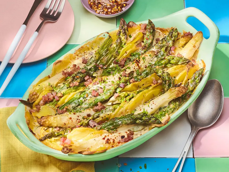 Spargel-Kartoffel-Gratin in einer grünen Auflaufform steht auf einem gedeckten Tisch.