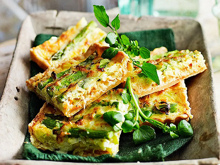 Quiche-Stücke mit grünem Spargel und frischen Kräutern liegen auf einem Tablett und sind bereit zum Mitnehmen.