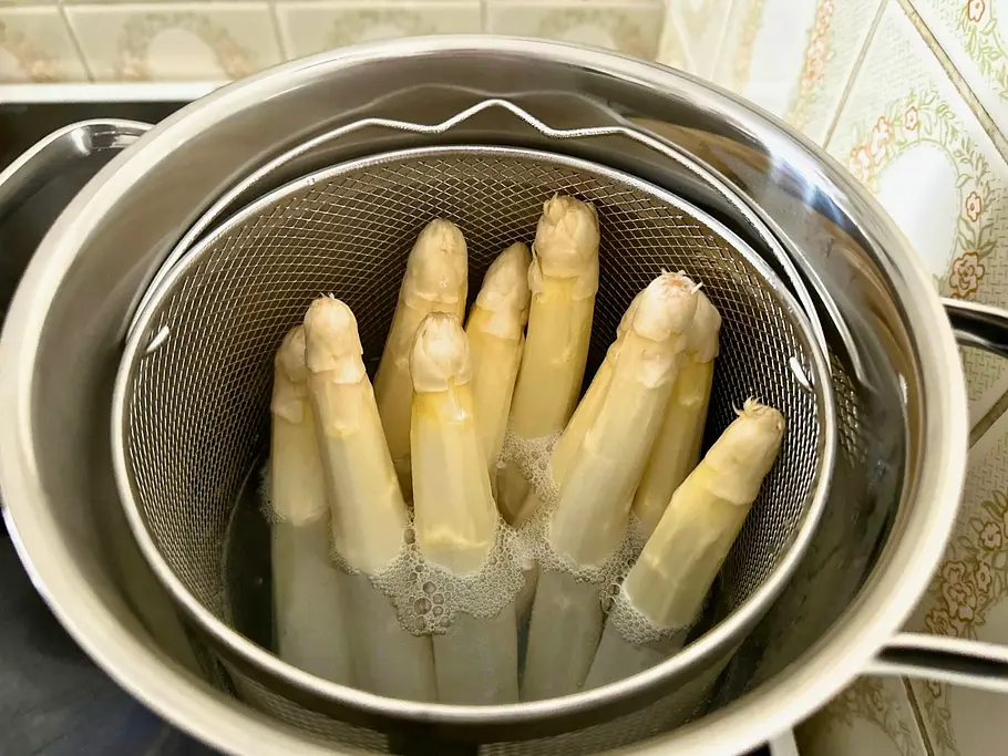 Spargeltöpfe im Vergleich Weißer Spargel kocht im Kocheinsatz des Spargeltopfes auf dem Herd.