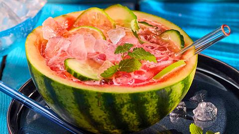 Wassermelonen-Limonade in einer ausgehöhlten Wassermelonen-Hälfte mit vielen Eiswürfeln und Gurkenscheiben-Deko. - Foto: House of Food / Bauer Food Experts KG