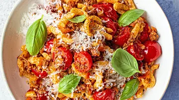 Spätzle mit Hackfleisch-Bolognese, Kirschtomaten und frisch geriebenem Parmesan, garniert mit Basilikum, angerichtet auf einem weißen Teller. - Foto: Simone Neufing/MOE‘S QUICK & EASY FOOD