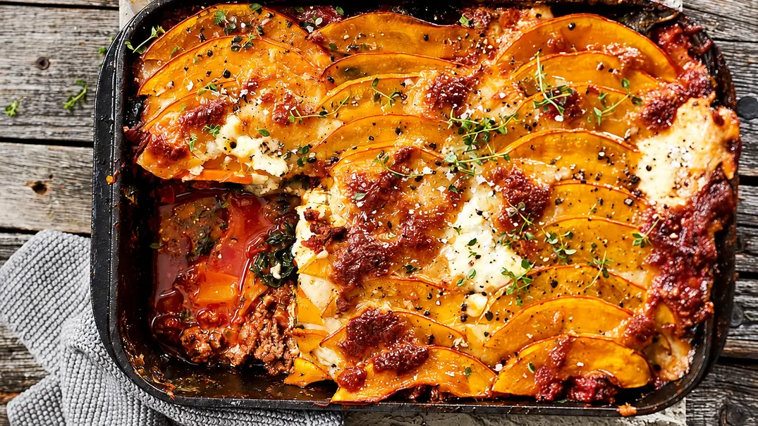 Spinat-Kürbis-Lasagne mit Käse und Kräutern steht in einer schwarzen Auflaufform auf einem Holztisch. Ein Stück fehlt. - Foto: LECKER @ Bauer Media Group Spinat-Kürbis-Lasagne mit Käse und Kräutern steht in einer schwarzen Auflaufform auf einem Holztisch. Ein Stück fehlt. - Foto: LECKER @ Bauer Media Group