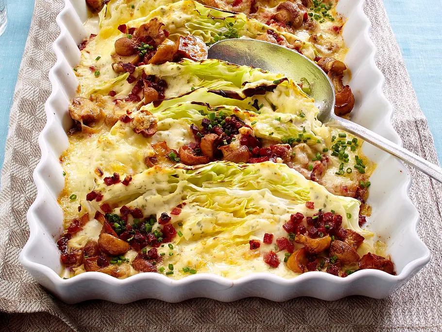 Spitzkohlspalten in Champignon-Käse-Rahm mit Speckwürfeln Rezept Spitzkohlspalten mit Champignons, Speck und cremiger Sauce liegen in einer weißen Auflaufform mit Servierlöffel.