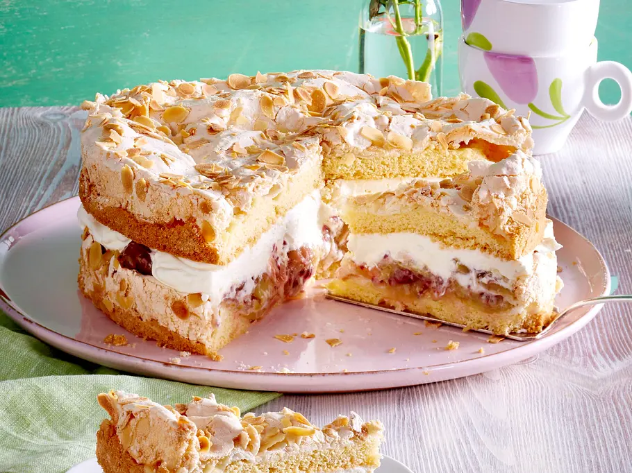 Unten und oben Baiserböden mit gehobelten Mandeln, dazwischen Sahne und Stachelbeerkompott: So präsentiert sich die angeschnittene Stachelbeer-Baiser-Torte auf einer rosa Tortenplatte.