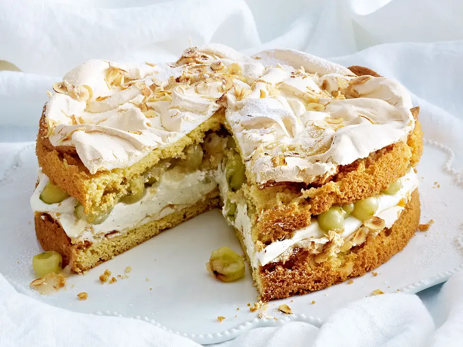 Stachelbeertorte mit Baiser Auf einem weißen Bettlaken steht eine angeschnittene Stachelbeertorte mit Sahnecreme in der Mitte und einem Topping aus knuspriger Baisermasse