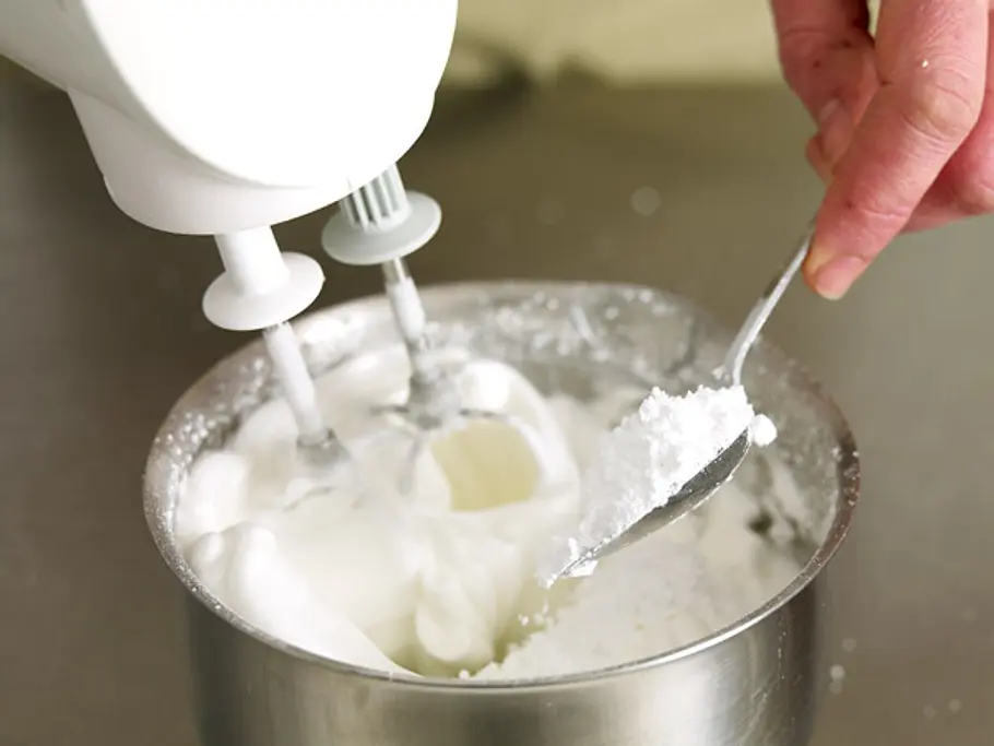 Eiweiß wird in einer Metallschüssel mit einem Handmixer zu steifem Schnee geschlagen, dabei wird nach und nach die Stärke-Zucker-Mischung mit einem Löffel zugegeben.