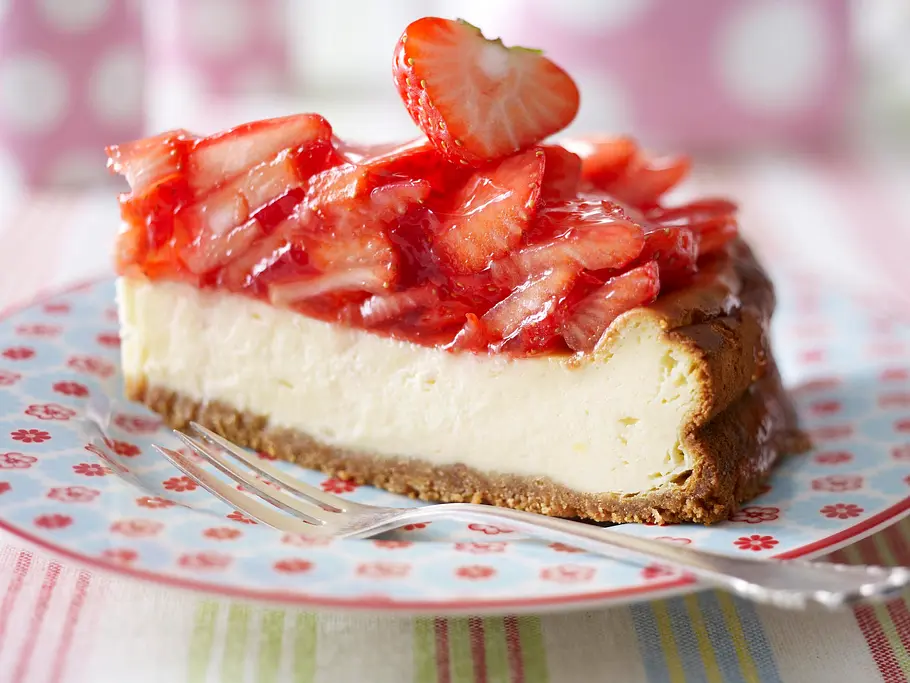 Strawberry-Cheesecake (Erdbeer-Käsekuchen) Ein Stück Strawberry-Cheesecake mit üppigem Erdbeer-Belag auf einem hellblauen Teller mit roten Blümchen, eine Kuchengabel liegt mit auf dem Teller.
