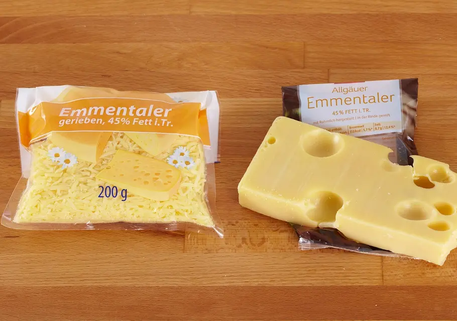 Eine Packung geriebener Emmentaler neben einer Packung mit Emmentaler am Stück