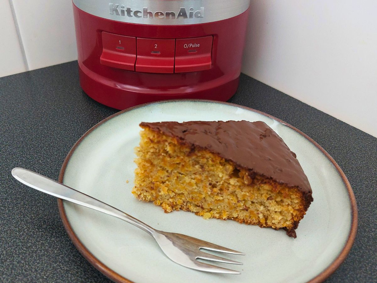 ein Stück Karottenkuchen mit KitchenAid Food-Processor im Hintergrund