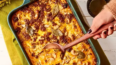 Südafrikanischer Hackfleischauflauf, goldbraun überbacken mit Cashewkernen und Lorbeerblättern, in einer rechteckigen Form serviert, dazu eine Schale mit leuchtend gelbem Reis. - Foto: LECKER @ Bauer Media Group