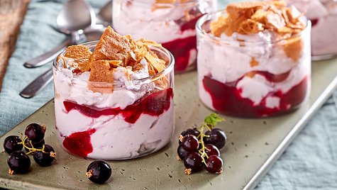 Vier Dessertgläser mit einer Schicht aus schwarzem Johannisbeerpüree und Sahne-Mascarpone-Creme, getoppt mit knusprigen Keksstücken, dekoriert mit frischen schwarzen Johannisbeeren auf einem Tablett. - Foto: House of Food / Bauer Food Experts KG