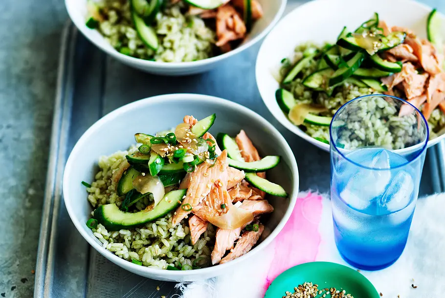 sushi-bowl-mit-matcha-reis-und-stremellachs Auf einem Tisch stehen drei Schüsseln mit grünem Matcha-Reis, Gurkensalat und zerzupftem Stremellachs als Sushi-Bowls.
