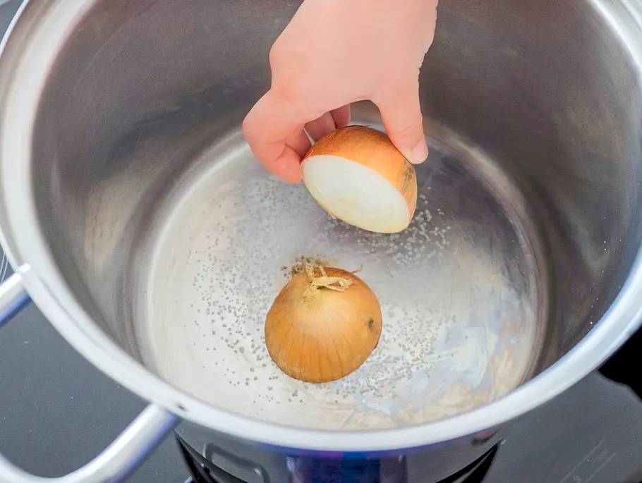 Halbierte Zwiebel wird mit der Schnittfläche nach unten in einem großen Topf ohne Fett angeröstet, grobes Salz ist bereits auf dem Topfboden verteilt.