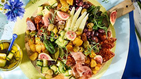 Eine bunte Platte mit Oliven, Schinken, Chorizo, Feigen, Käse, gegrilltem Gemüse und frischen Kräutern steht auf einem Tisch. - Foto: House of Food / Bauer Food Experts KG