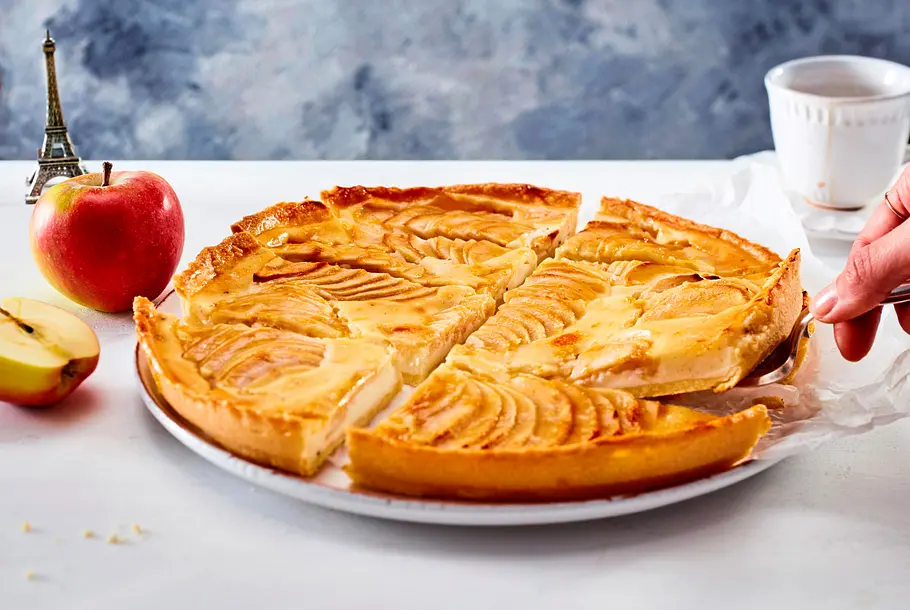 Französischer Käsekuchen mit Äpfeln belegt und in Stücke geschnitten. Ein Stück wird herausgehoben.