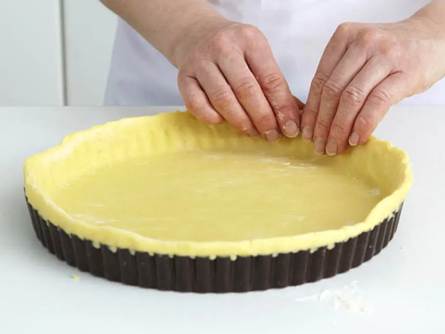Eine Tarteform ausgelegt mit Teig und zwei Hände, die den Teig am Rand festdrücken.