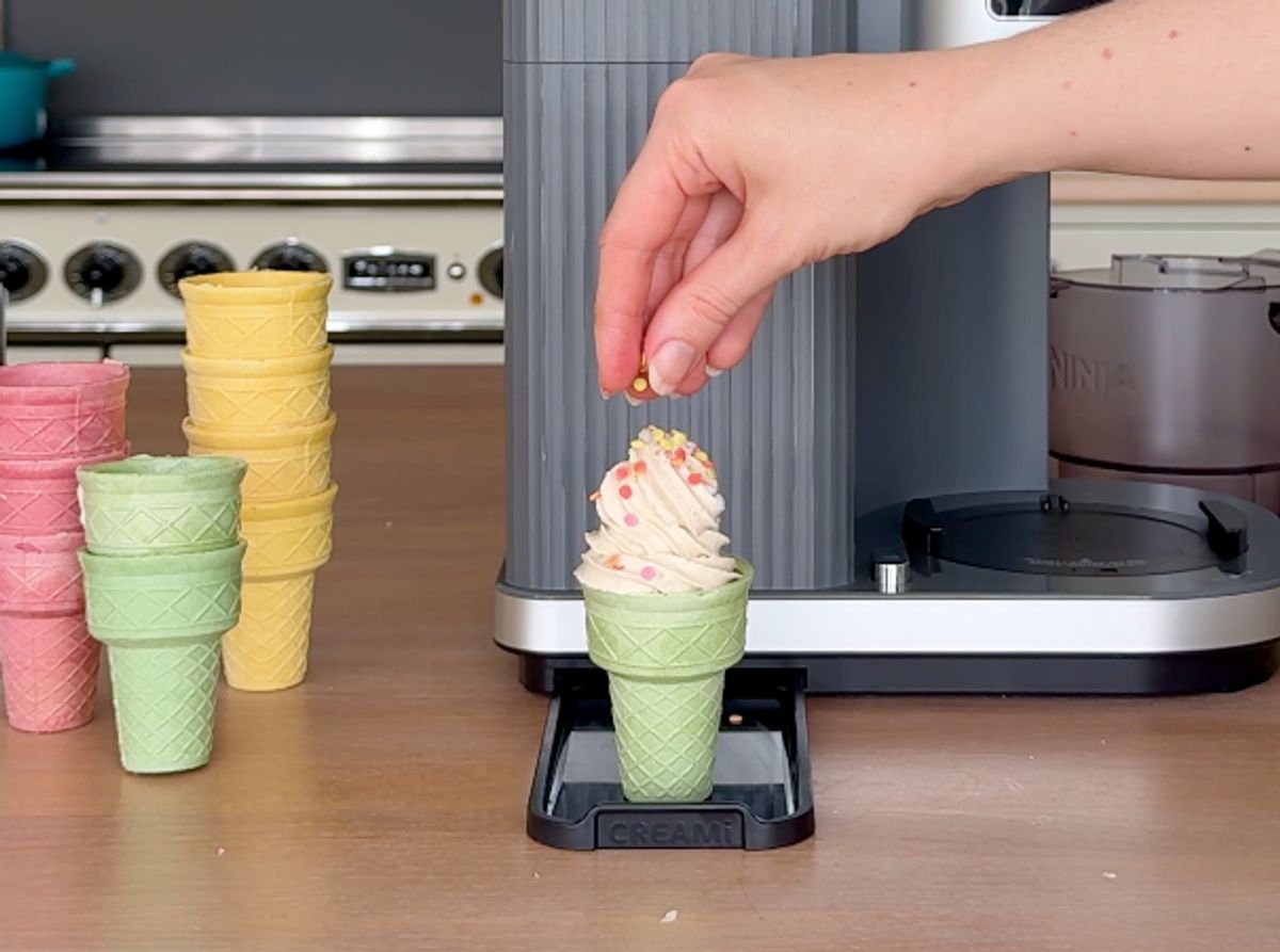 Eine Hand dekoriert ein fertiges Softeis aus der Ninja Swirl mit Streuseln