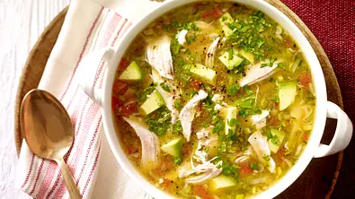 Hühnersuppe mit zarten Hähnchenstreifen, Avocadowürfeln, Tomaten und frischen Kräutern, serviert in einer weißen Schale auf einem runden Holzbrett mit goldener Löffel und ein paar Tortillachips als Beilage. - Foto: LECKER @ Bauer Media Group Hühnersuppe mit zarten Hähnchenstreifen, Avocadowürfeln, Tomaten und frischen Kräutern, serviert in einer weißen Schale auf einem runden Holzbrett mit goldener Löffel und ein paar Tortillachips als Beilage. - Foto: LECKER @ Bauer Media Group