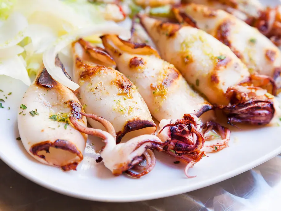 Gegrillter Tintenfisch auf einer Servierplatte Fünf goldbraun gegrillte Tintenfischtuben und -tentakel auf einer Servierplatte