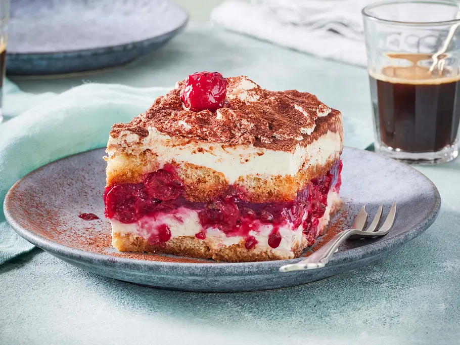 Tiramisu-Kirsch-Schnitten Rezept Eine Tiramisu-Kirsch-Schnitte liegt mit Kakao bestäubt auf einem Teller.