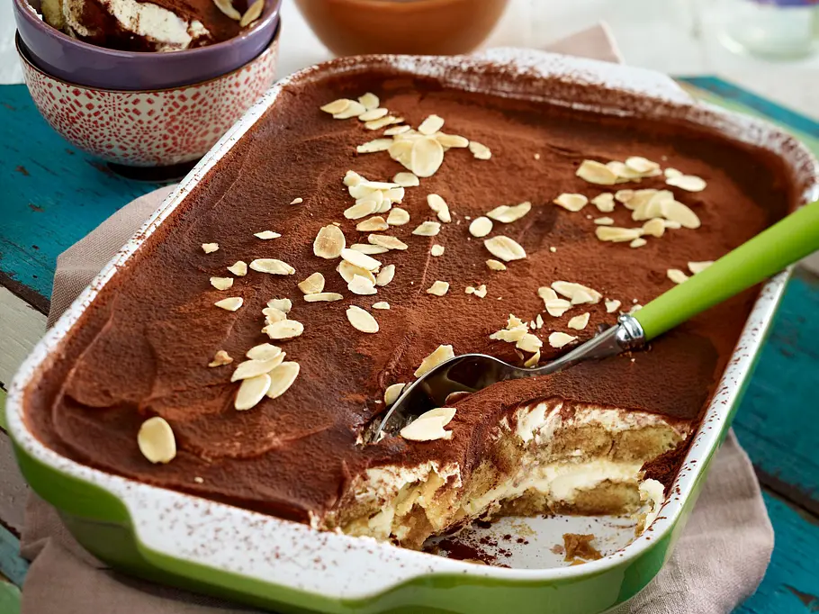 Angeschnittenes Tiramisu ohne Ei mit cremiger Quark-Mascarpone-Creme und Kakaopulver in einer grünen Auflaufform