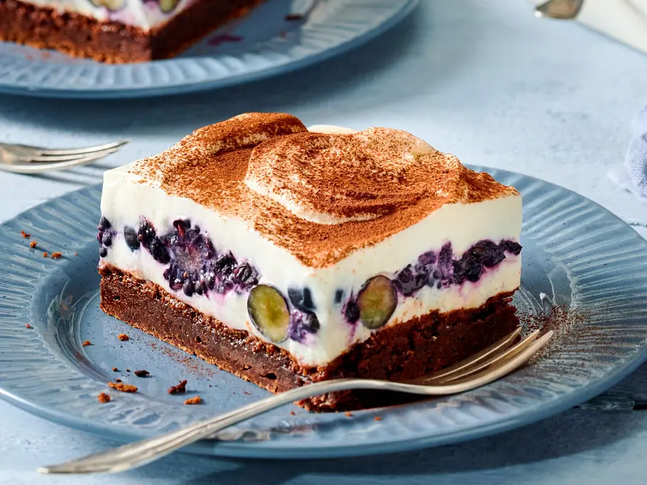 Tiramisu-Schnitten mit Brombeeren und Heidelbeeren Tiramisu-Schnitte mit Brombeeren und Heidelbeeren auf einem blauen Teller, auf den eine silberne Kuchengabel liegt.