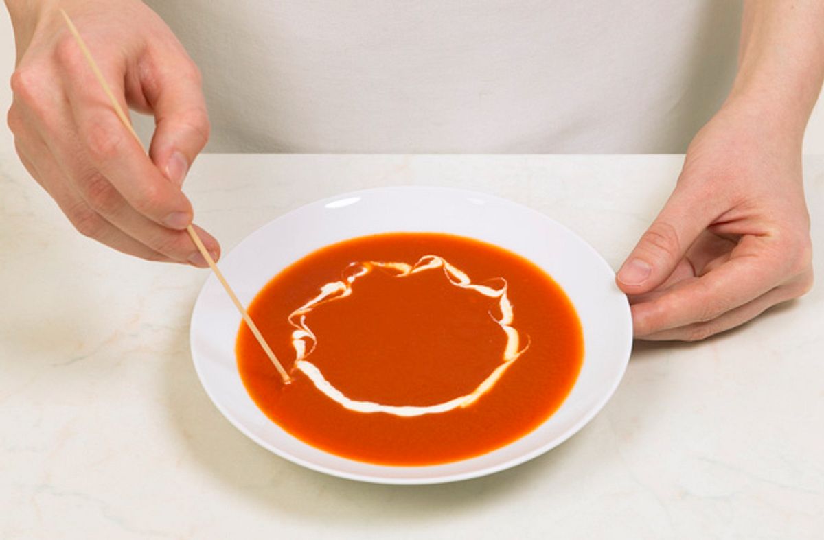 Tomatensuppe garnieren Sie am besten mit etwas Sahne, die Sie mit einem Holzstäbchen zu einem Muster ziehen.