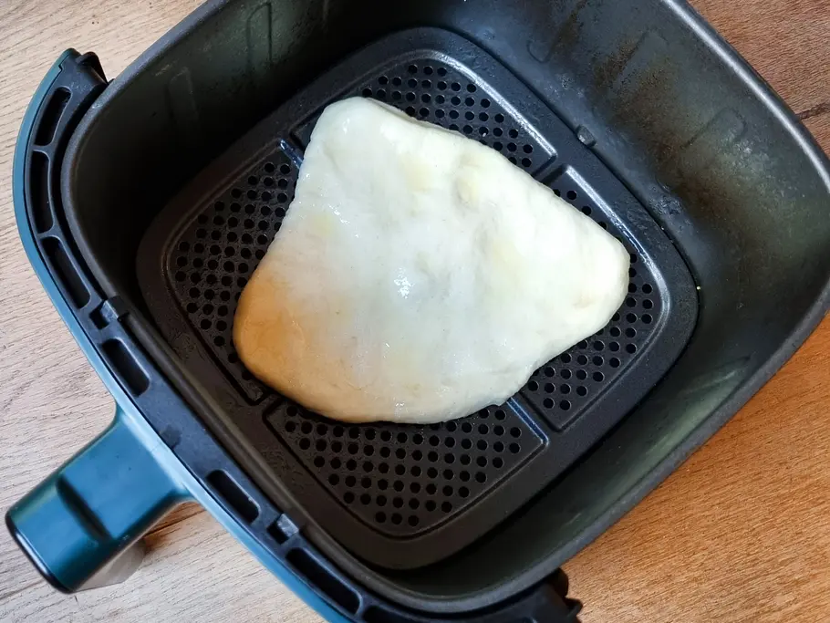 Langos-Teigling liegt als Fladen im Garkorb eines Airfryers.