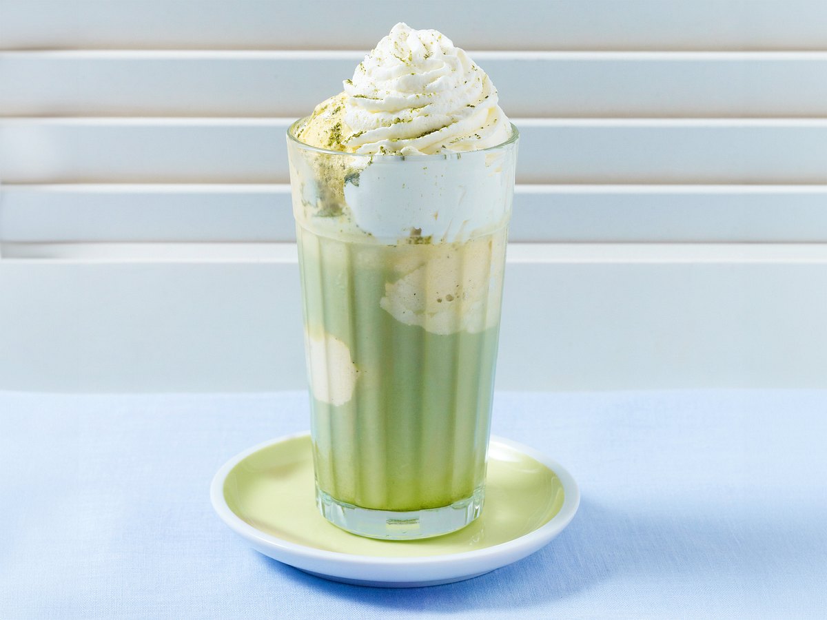 Matcha Latte mit Vanilleeis und Sahnehaube in einem großen Glas. Mit im Bild Redakteurin Birte.