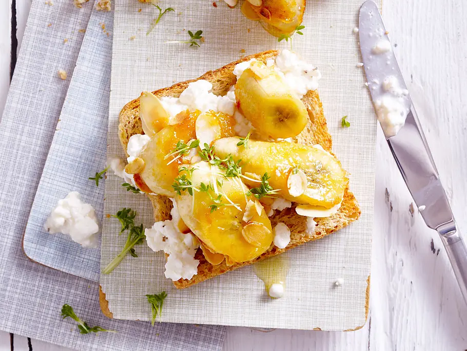 Vollkorntoast mit Hüttenkäse und Banane Vollkorntoast auf einem Frühstücksbrett mit Hüttenkäse, Banane und Kresse.