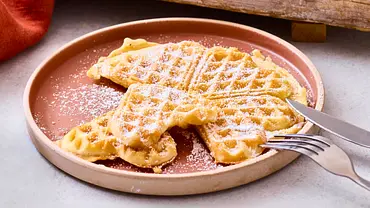 Auf einem rosa Teller liegt eine saftig aussehende Herzwaffel, die mit Puderzucker bestäubt ist - Foto: LECKER @ Bauer Media Group Auf einem rosa Teller liegt eine saftig aussehende Herzwaffel, die mit Puderzucker bestäubt ist - Foto: LECKER @ Bauer Media Group