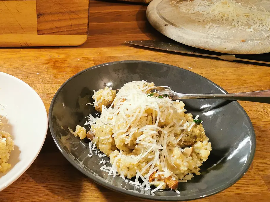 Resikcoher-Risotto mit Pilzen und Parmesan Waldpilz-Risotto mit Parmesan angerichtet auf einem dunklen Teller mit Gabel.