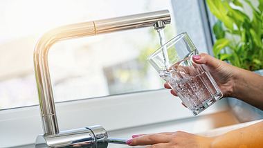 Eine Frau hält ein Glas Wasser unter den laufenden Wasserhahn - Foto: iStock/rclassenlayouts