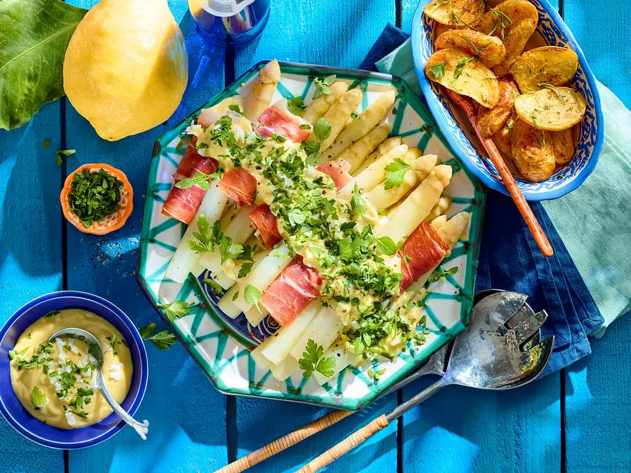 Weißer Spargel mit Bozener Soße Rezept Weißer Spargel, Schinkenröllchen und Bozener Soße mit frischen gehackten Kräutern auf einem blau-weiß gemusterten Teller