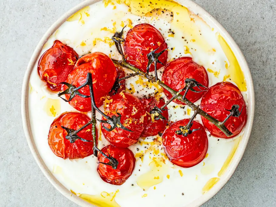 Whipped Feta Italien Style Rezept Cremig aufgeschlagener Feta serviert in einer flachen, hellen Schale, getoppt mit gerösteten Kirschtomaten am Zweig, verfeinert mit Olivenöl und Zitronenzesten.