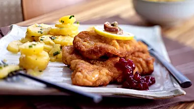 Zwei Wiener Schnitzel mit einer Scheibe Zitrone, Kartoffelsalat und Preiselbeermarmelade auf einem weißen Teller - Foto: LECKER @ Bauer Media Group