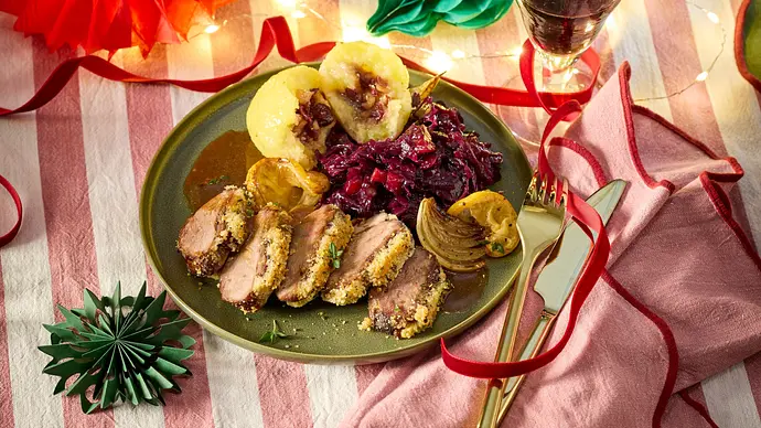 In Scheiben geschnittene Filets mit knuspriger Thymian-Kräuterkruste auf einem grünen Teller, daneben zwei gefüllte Klöße, Rotkohl und Bratensauce, serviert auf einer gestreiften Stoffdecke. - Foto: LECKER @ Bauer Media Group In Scheiben geschnittene Filets mit knuspriger Thymian-Kräuterkruste auf einem grünen Teller, daneben zwei gefüllte Klöße, Rotkohl und Bratensauce, serviert auf einer gestreiften Stoffdecke. - Foto: LECKER @ Bauer Media Group