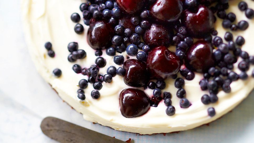 Ziegenfrischkäsetorte mit Süßkirschen und Blaubeeren, seitlich liegt ein Kuchenmesser - Foto: House of Food / Bauer Food Experts KG