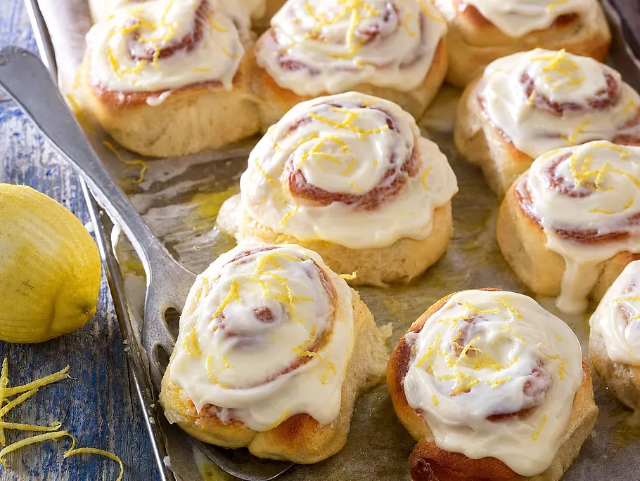 Zitronen-Hefeschnecken Saftige Zitronenschnecken mit cremigem Frischkäsefrosting und frischer Zitronenschale auf einem Backblech.