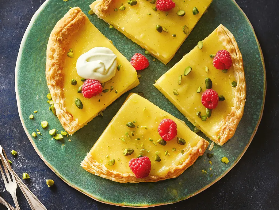 Zitronentarte mit Pistaziensahne Zitronentarte mit Pistaziensahne aus dem Airfryer, in 4 Stücke geschnitten und mit Himbeeren dekoriert.