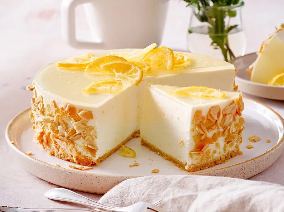 Zitronentorte aus Frischkäse dekoriert mit Zitronenscheiben und Eiswaffelstückchen am Rand mit dünnem Knusperboden auf einem modernen  weißen Teller mit Rand